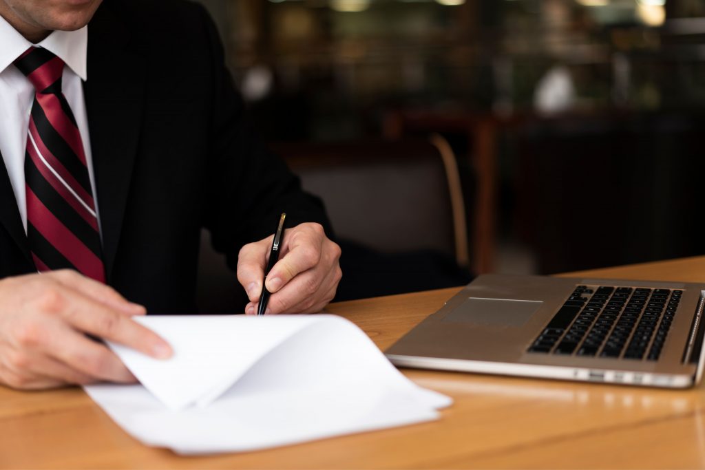 man in suit signing papers on desk